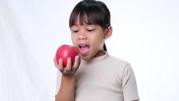 niña feliz con manzana. Linda niña asiática comiendo manzana orgánica sobre fondo blanco en el estudio. nutrición saludable para niños pequeños. video