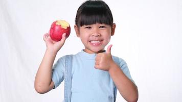 niña feliz con manzana. Linda niña asiática comiendo manzana orgánica sobre fondo blanco en el estudio. nutrición saludable para niños pequeños. video