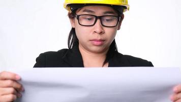 arquiteta feminina em um capacete olhando planos de construção em um fundo branco em estúdio. mulher bonita engenheira civil olhando a planta e examinando o mapa de rascunho. video