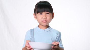 linda niña desayunando. niña feliz comiendo cereal con leche del tazón sobre fondo blanco en el estudio. nutrición saludable para los niños. video