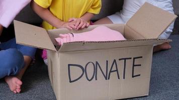 duas irmãs adoráveis com sua mãe colocando suas roupas em caixa de doação em casa para ajudar os pobres. conceito de doação. video