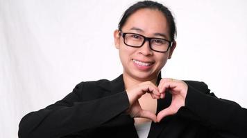 linda empresária asiática sorrindo e mostrando uma forma de coração com as mãos no fundo branco no estúdio. video