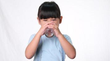 schattig klein Aziatisch meisje drinkwater uit een glas en duimen opdagen op een witte achtergrond in de studio. goede gezonde gewoonte voor kinderen. gezondheidszorg concept video