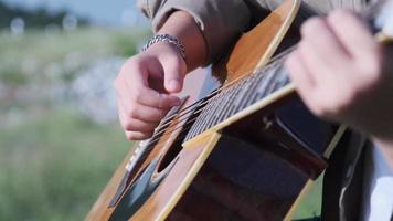 un apuesto hombre asiático de pelo rizado tocando la guitarra y cantando junto al lago al atardecer de vacaciones. video