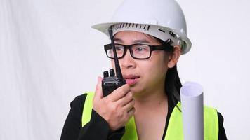Female civil engineer in a helmet holding construction plans and using walkie-talkie and talk to other staff on a white background in studio. video