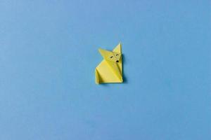 un zorro de origami está doblado de papel amarillo en la técnica de origami con ojos pintados, nariz. en medio del fondo azul. concepto de amor por los animales, pasatiempos, actividades con niños. foto
