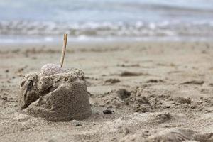 montaña de arena con un palo de madera en la playa a orillas del mar. castillo de arena con una piedra en la playa. primer plano de pequeños castillos de arena con un palo rematado contra un cielo azul foto