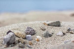 Sand mountain on the beach full of stones, blurry sea, and sand background. a pile of nice beach sand with and stones
