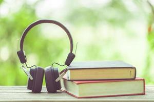 Book and black headphone on wooden table with abstract green nature blur background. Reading and education concept