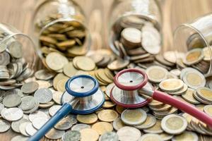 Blue stethoscope and jar of coin on wooden table. Money and financial checking concept photo