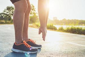 concepto de bienestar de entrenamiento de hombre pies de corredor con zapatillas deportivas corriendo en la carretera en el parque. centrarse en el zapato. filmado en la mañana, luz solar y efecto cálido con espacio de copia para texto o diseño foto