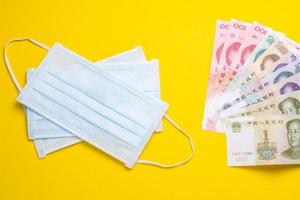 Chinese banknote and new white mask on yellow. Mask is important but lack and very expensive in many country of Virus situation in 2020 photo