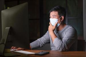 hombre con mascarilla preventiva y trabajando desde casa por la noche en situación de enfermedad por el virus de la corona. trabajo desde casa y concepto saludable foto