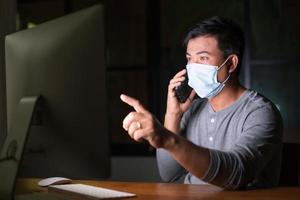 hombre con mascarilla preventiva y trabajando desde casa por la noche en situación de enfermedad por el virus de la corona. trabajo desde casa y concepto saludable foto