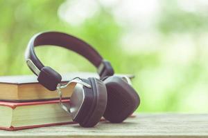 Book and black headphone on wooden table with abstract green nature blur background. Reading and education concept photo