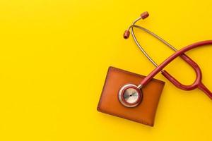 estetoscopio médico y la nueva billetera de cuero marrón para hombres sobre fondo amarillo. presupuesto para control de salud o dinero y concepto financiero foto