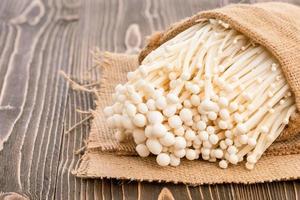 champiñón de aguja dorado fresco blanco o hongo enoki en saco sobre tablón de madera marrón foto