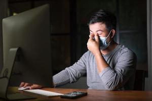 hombre con mascarilla preventiva y trabajando desde casa por la noche en situación de enfermedad por el virus de la corona. trabajo desde casa y concepto saludable foto