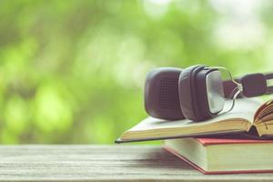Book and black headphone on wooden table with abstract green nature blur background. Reading and education concept photo