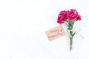 May mothers day idea concept photography - Beautiful blooming carnations tied by bow with kraft text card isolated on bright modern table, copy space, flat lay, top view, mock up photo