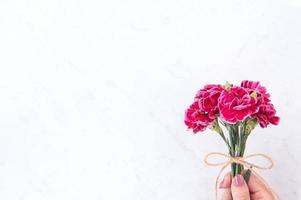 fotografía conceptual de la idea del día de las madres: hermosos claveles florecientes atados por un lazo de cuerda sosteniendo en la mano de una mujer aislada en una mesa moderna y luminosa, espacio para copiar, endecha plana, vista superior foto