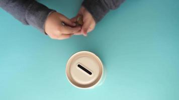 child hand saving coins in a container on light green background top view video