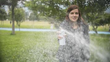 mujer hispana disparando un chorro de espuma blanca de una lata de aerosol en medio de un parque foto