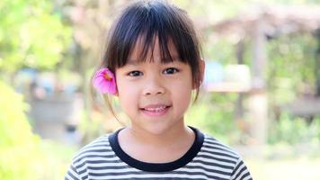 Cute little Asian girl with pink flower on ear. Childhood happiness concept. video