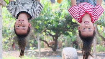Two cute Asian siblings hanging upside down on the trees in the garden. Happy children are happily climbing on the tree. video