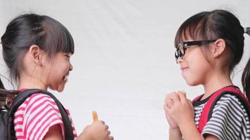 Friendly cheerful classmates sharing healthy meal. Two cute schoolgirls having lunch together on white background in studio. Concept of nutrition in school. video