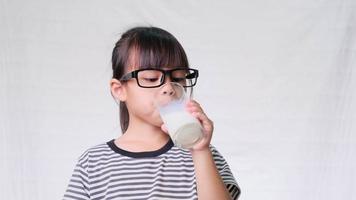 linda niña bebiendo leche de un vaso sobre fondo blanco. nutrición saludable para los niños. video