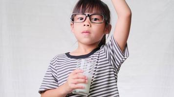 bambina carina con un bicchiere di latte su sfondo bianco. alimentazione sana per i bambini. video