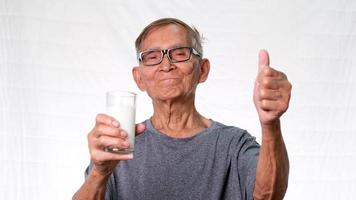 gezonde oude man met een glas melk met duimen omhoog op een witte achtergrond in de studio.