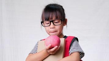 schoolmeisje blij met beurt en rode appel in de hand op een witte achtergrond in de studio. een gezonde snack op school, rode appels in de pauze op school. concept van voeding op school. video