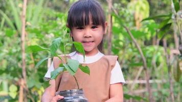 linda niñita sosteniendo un árbol pequeño en una olla de reciclaje sobre un fondo verde borroso en primavera. concepto de ecología del día de la tierra