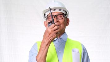Senior architect engineering builder wearing safety vest and helmet using walkie-talkie talks about work on white background in studio. video