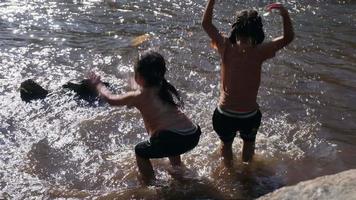 menina asiática brincando no córrego da floresta com a irmã. recreação ativa com crianças no rio no verão. video