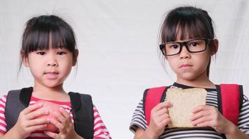 Friendly cheerful classmates sharing healthy meal. Two cute schoolgirls having lunch together on white background in studio. Concept of nutrition in school. video