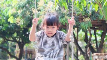 Smiling little girl playing on a swing in the summer garden. video