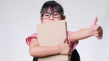 Smiling schoolgirl wearing summer outfit with backpack holding books on white background in studio. Back to school concept video