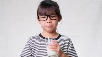 Cute little girl drinking milk from a glass on white background. Healthy nutrition for children.