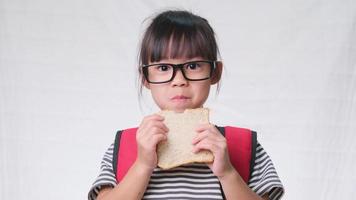 schattig schoolmeisje na de lunch op school. schattig klein meisje met brood op een witte achtergrond in de studio. concept van voeding op school. video