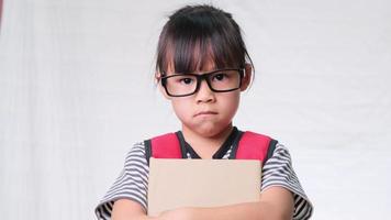 Smiling schoolgirl wearing summer outfit with backpack holding books on white background in studio. Back to school concept video