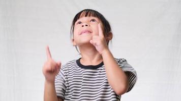 Cute little girl looking and pointing up to empty place with both hands over a white studio background. video