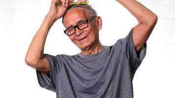 Elderly man combing hair with green comb on white background in studio. video