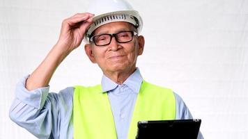 architetto senior di ingegneria edile che indossa un giubbotto e un casco tiene una tavoletta digitale su sfondo bianco in studio. video