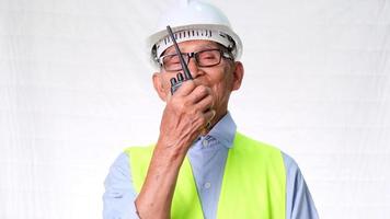 Senior architect engineering builder wearing safety vest and helmet using walkie-talkie talks about work on white background in studio. video