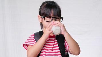 linda colegiala bebiendo leche de un vaso antes de ir a la escuela. nutrición saludable para los niños. concepto de regreso a la escuela video