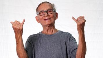 Funny grandfather in gray t-shirt and glasses showing hand gesture on white background in studio.