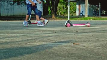 Two cute little girls riding scooter on road in park outdoors on summer day. Kids play outdoors with scooters. Active leisure and outdoor sport for child video